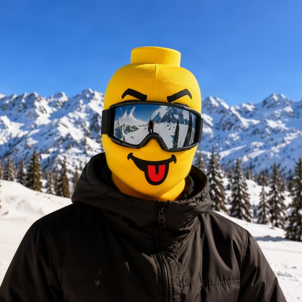 Lifestyle hero: a skier on a snowy mountain wearing the yellow brick-head smiley mask with ski goggles, grinning at the camera